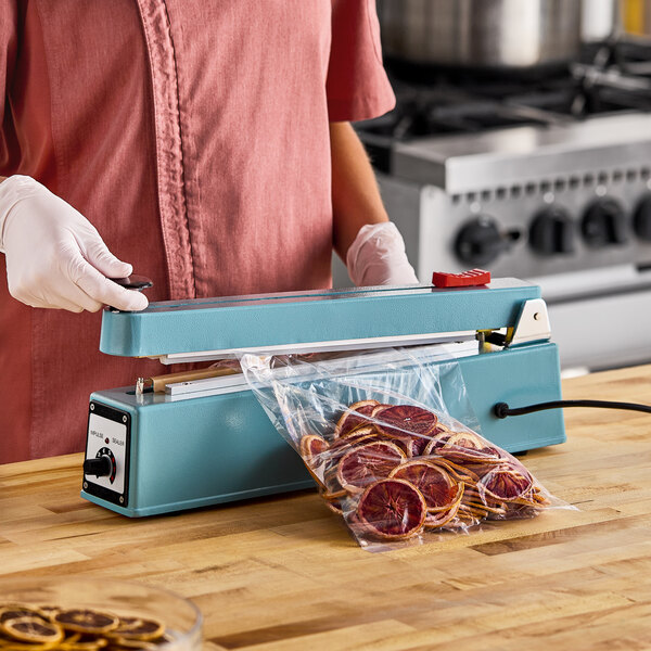 A blue 12-inch impulse heat bag sealer with a cutter and timer being used to seal a plastic bag of dried citrus slices.