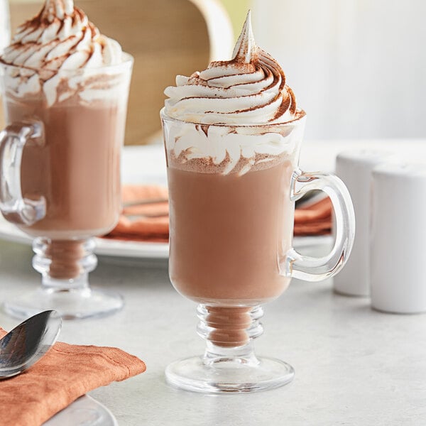Two Acopa Select Irish coffee mugs filled with hot chocolate and whipped cream.