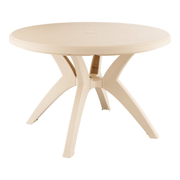 A sandstone round Grosfillex Ibiza table with four legs on an outdoor patio.