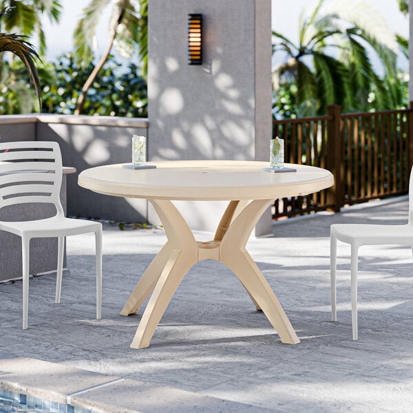 A Grosfillex Ibiza sandstone round pedestal table with chairs and an umbrella by a pool.