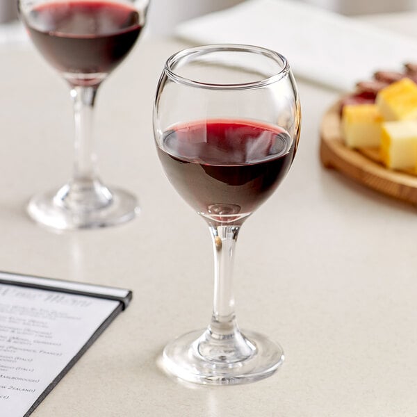 Two Acopa wine glasses filled with red wine on a table.