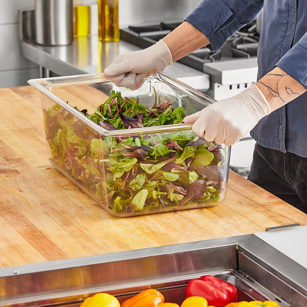 A person in gloves using a Vollrath clear plastic food pan to hold lettuce at a salad bar.