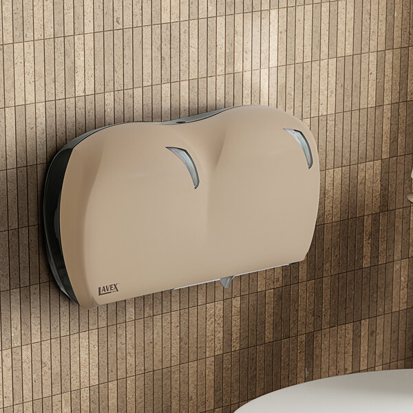 A Lavex Pro Sand double-roll jumbo toilet tissue dispenser mounted on a tan tile wall.