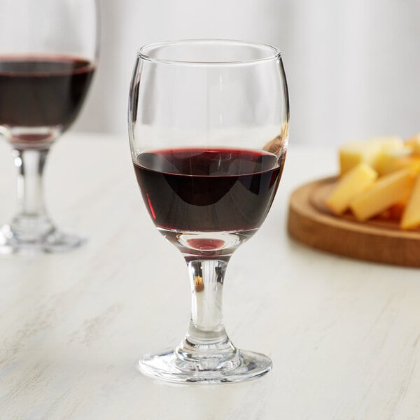 Two Acopa 16 oz. glass goblets of red wine next to a plate of cheese on a table.