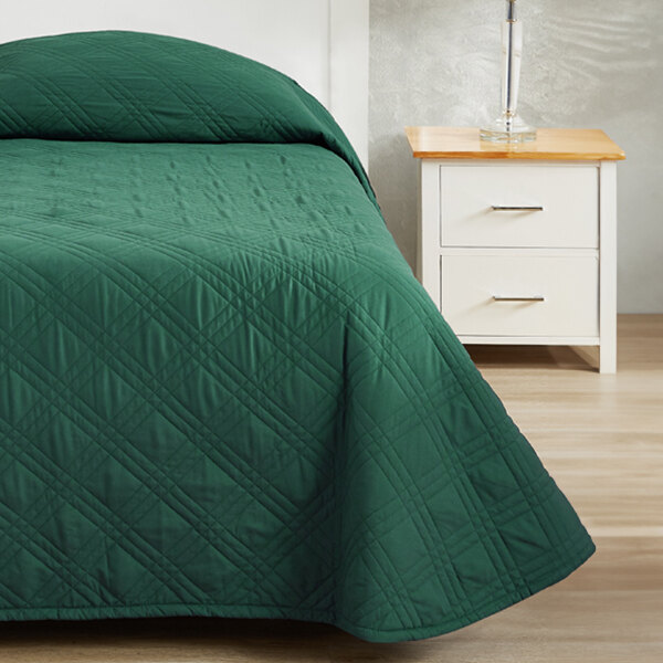 A green Berkshire Hospitality bedspread on a bed next to a white nightstand.