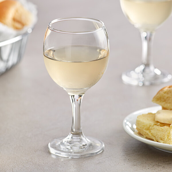 An Acopa all-purpose wine glass filled with white wine next to a plate of food.
