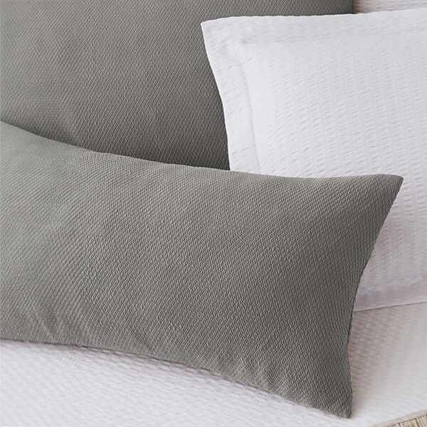 A close up of a smoke grey Berkshire Hospitality knit2fit diamond throw pillow on a bed.