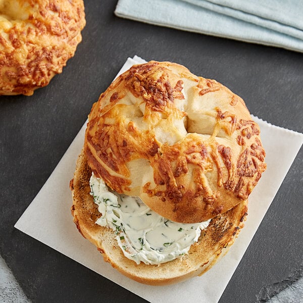 A close up of a Tribute Baking Company Asiago Cheese Bagel with cream cheese on top.