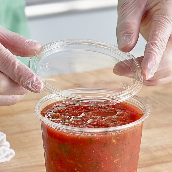 A person putting a Choice plastic lid on a plastic container of red liquid.