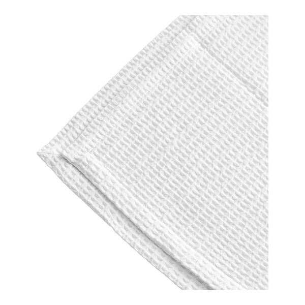 A close-up of a white Berkshire Hospitality pucker jacquard top sheet with a corner folded over.