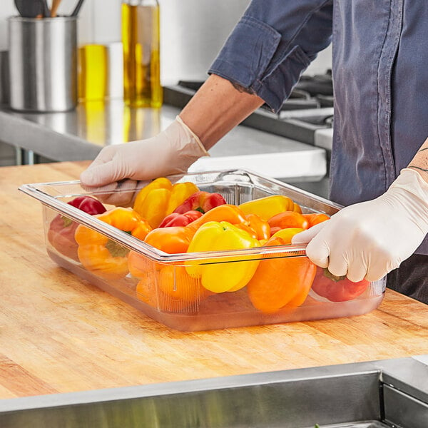 A person in gloves using a Vollrath clear polycarbonate food pan to hold yellow and red bell peppers.