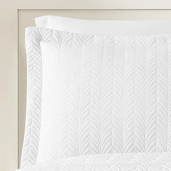 A white standard/queen size pillow sham with a quilted botanical leaf pattern.