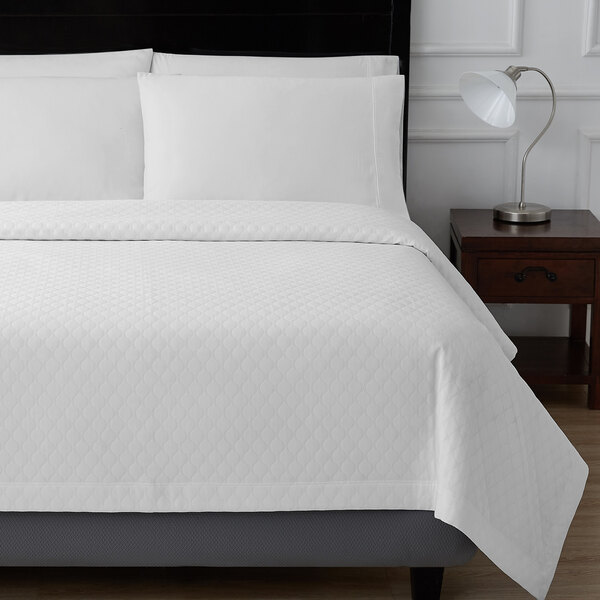 A white bed with a Berkshire Hospitality True White Ogee Matelasse coverlet on top.