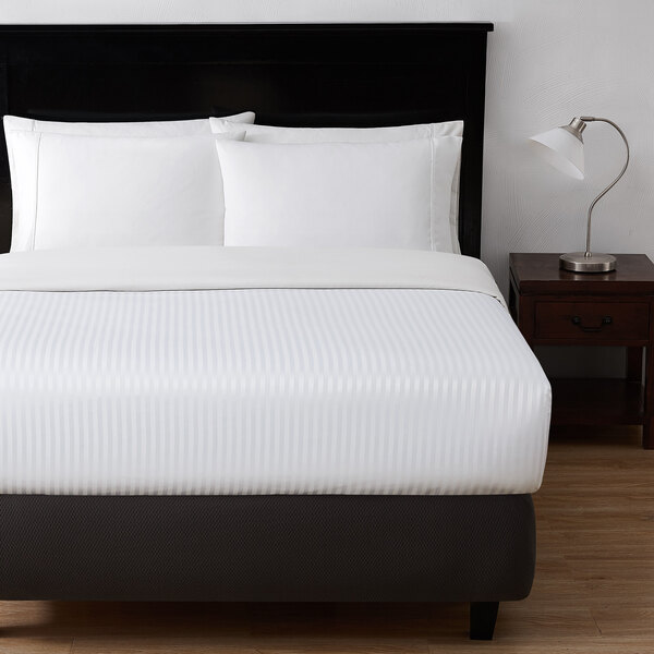 A king size bed made with white Berkshire Hospitality Soft Microfiber top sheet with pillows on it.
