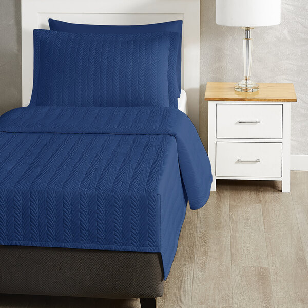 A blue Berkshire Hospitality quilt with a botanical leaf design on a bed.