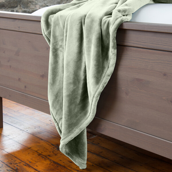 A green Berkshire Hospitality VelvetLoft throw blanket on a bed.