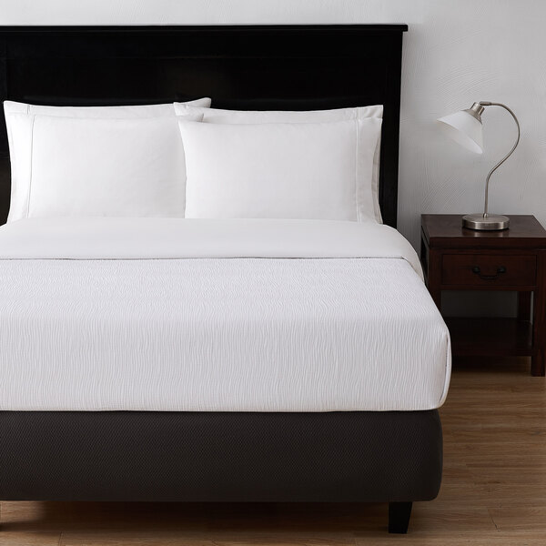 A white bed with a Berkshire Hospitality white ripple weave puff jacquard top sheet on it.