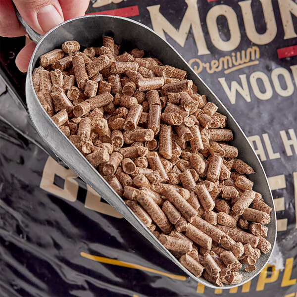 A person holding a metal cup with a scoop of Bear Mountain maple wood pellets.