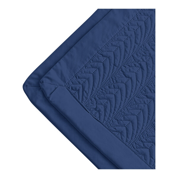 A white quilted coverlet with a blue botanical leaf pattern.