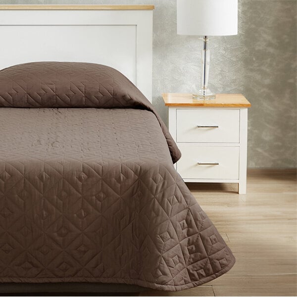A brown Berkshire Hospitality CozyCare Designs bedspread on a bed with a white nightstand.