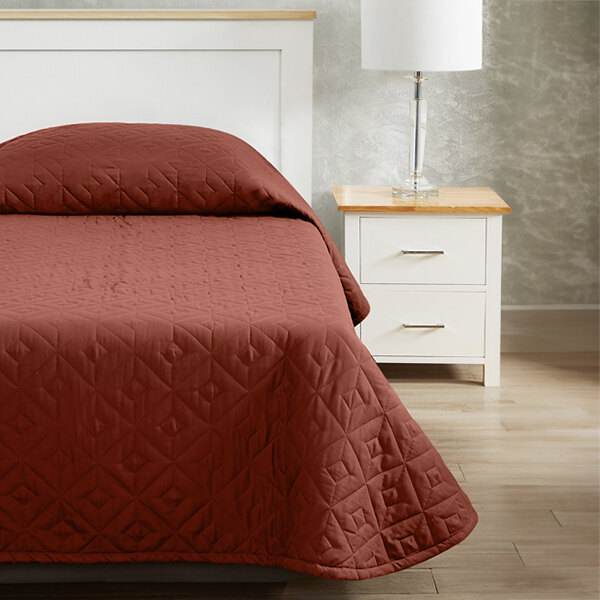 A bed with a nutmeg CozyCare Designs bedspread on a white bed with a nightstand.