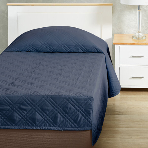A twin size bed with a navy blue Berkshire Hospitality CozyCare fitted coverlet.