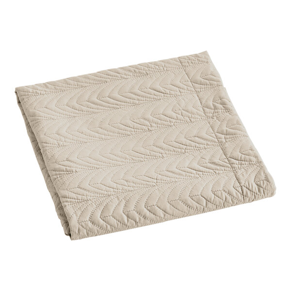 A folded sand colored Berkshire Hospitality quilted pillow sham with a botanical leaf pattern.