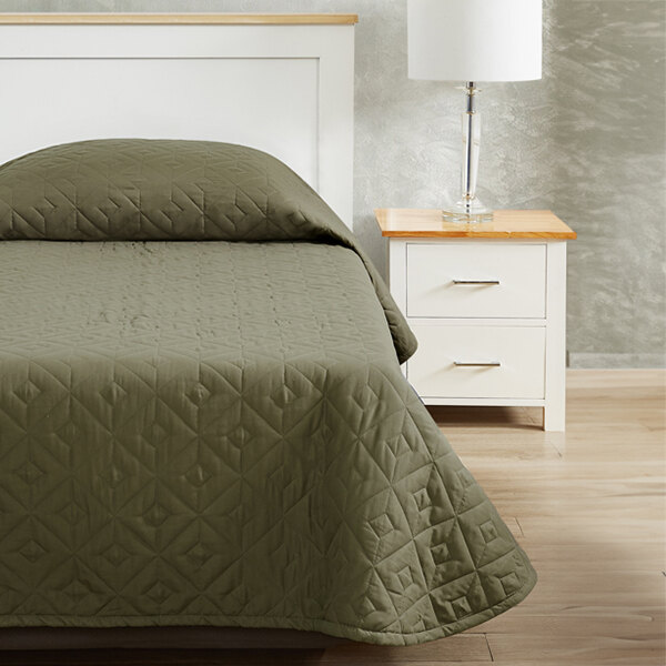 A white bed with a green Berkshire Hospitality CozyCare Designs bedspread on a white bed.