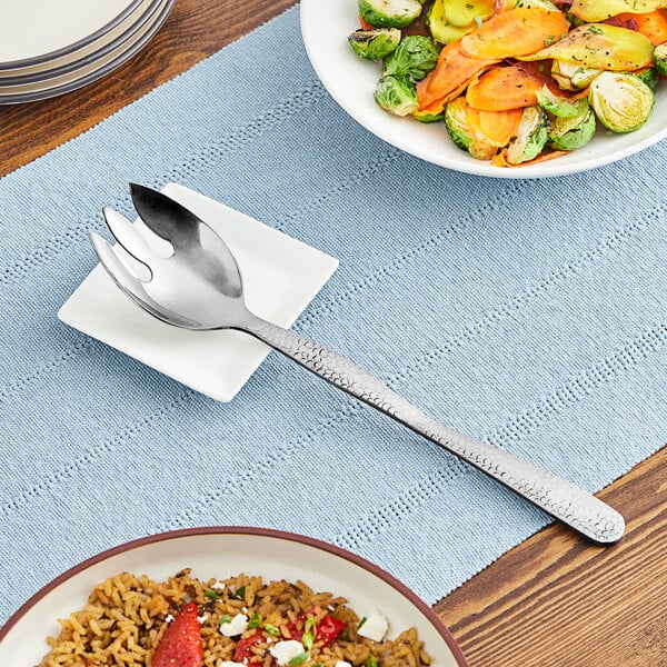 A plate of rice and vegetables with an American Metalcraft hammered stainless steel notched spoon on the table.