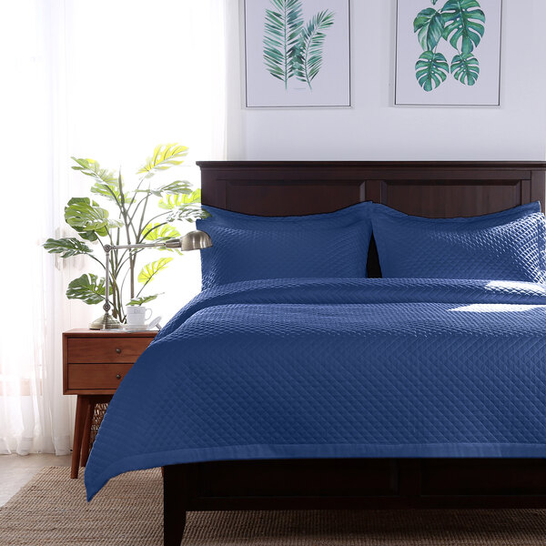 A bed with a Berkshire Hospitality Persian Blue quilted bedspread and a plant in front of it.