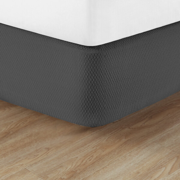 A close up of a bed with a white Berkshire Hospitality knit2fit diamond box spring cover on the mattress.