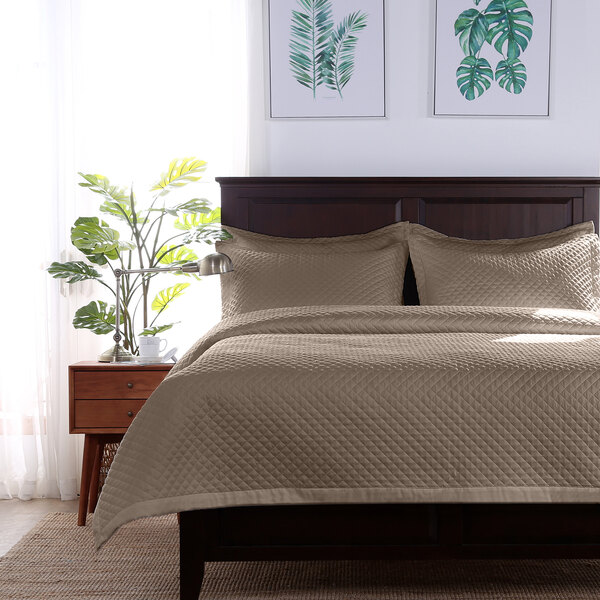 A bed with a Berkshire Hospitality twin size truffle diamond quilt bedspread and a plant on the side table.