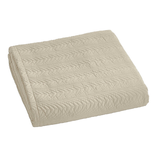A close-up of a sand colored Berkshire Hospitality quilted bedspread with a botanical leaf pattern.