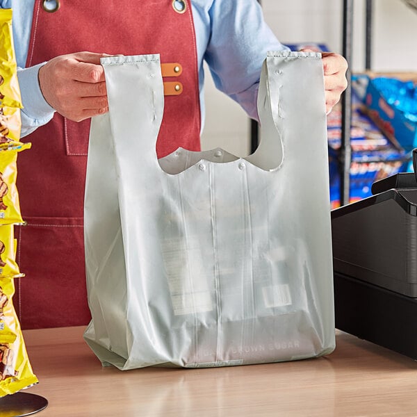 A person holding a Choice gray plastic T-shirt bag in front of a cash register.