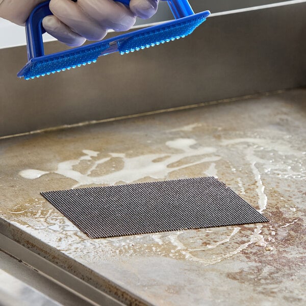 A rectangular grill screen being used to clean a flat grill surface.