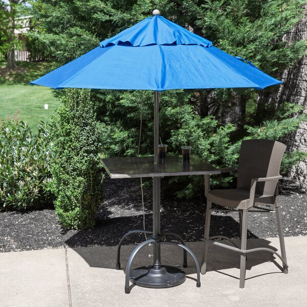 A table and chair under a Grosfillex Pacific Blue umbrella with a metal pole.