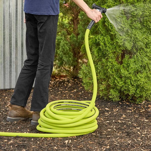 A person holding a Regency reinforced rubber hose with stainless steel connections and spraying water.