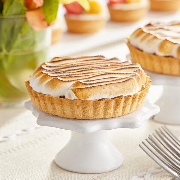 Two small sweet butter tart shells with meringue on top on a table in a bakery display.