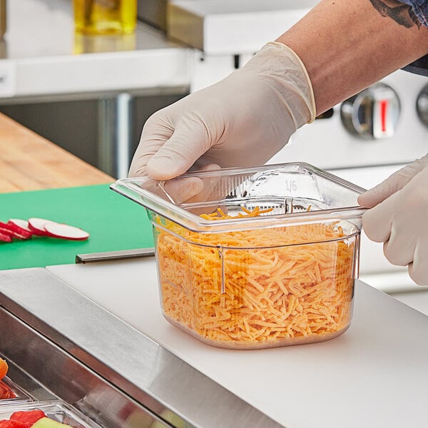 A person in gloves putting shredded cheese into a Vollrath clear plastic food pan.