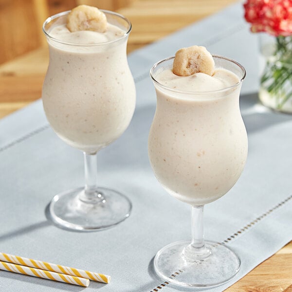 Two glasses of milkshakes with banana slices on top.