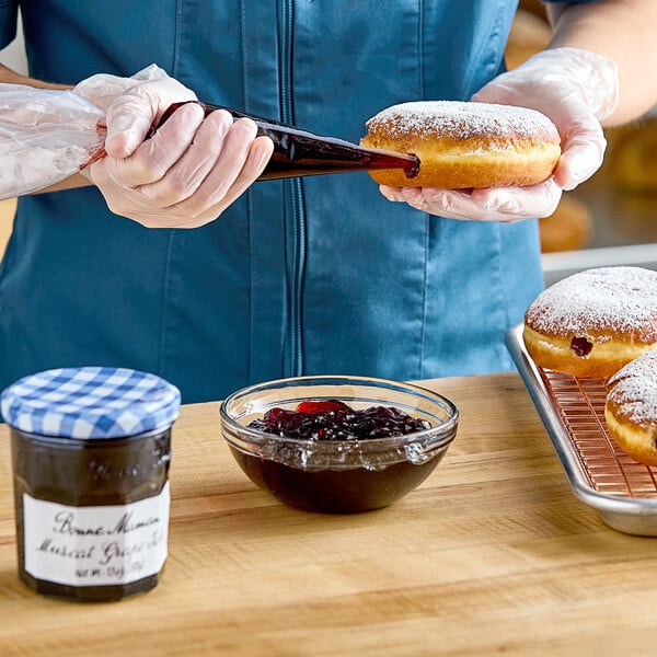 A person pouring Bonne Maman Muscat Grape jelly onto a donut.
