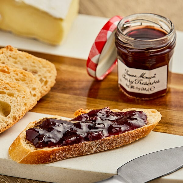 A piece of bread with Bonne Maman Cherry Preserves on a table next to a jar of jam and a knife.