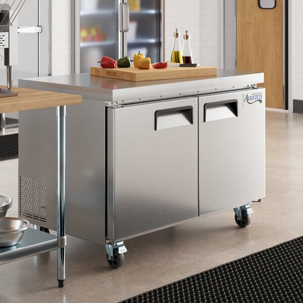 An Avantco stainless steel undercounter refrigerator on a counter with a cutting board on top.