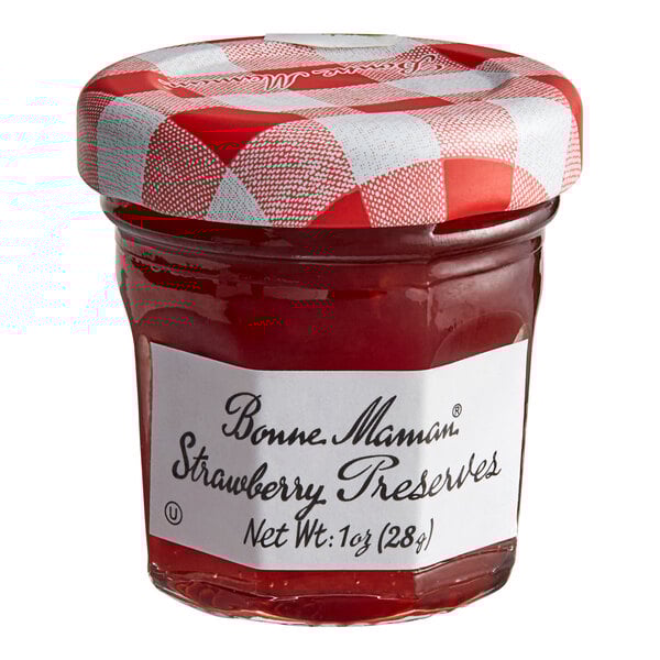 A Bonne Maman mini jar of strawberry preserves with a white label and red and white checkered lid on a table.