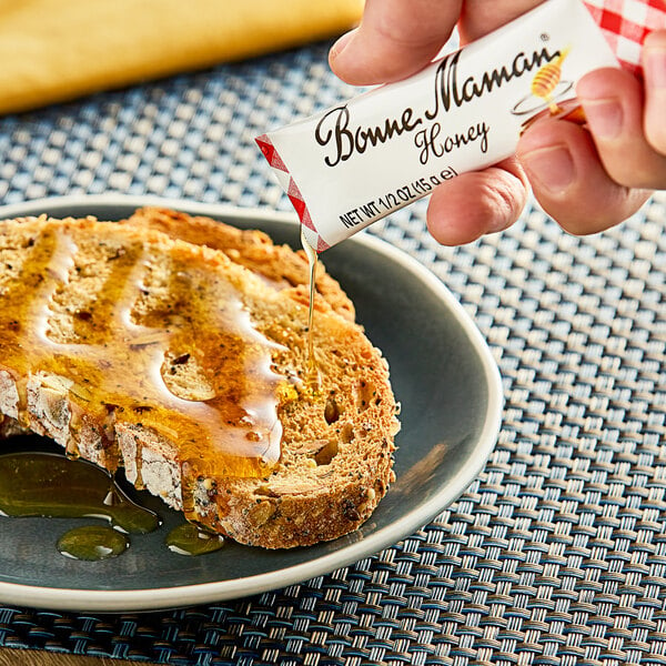 A person holding a small package of Bonne Maman honey on a plate.