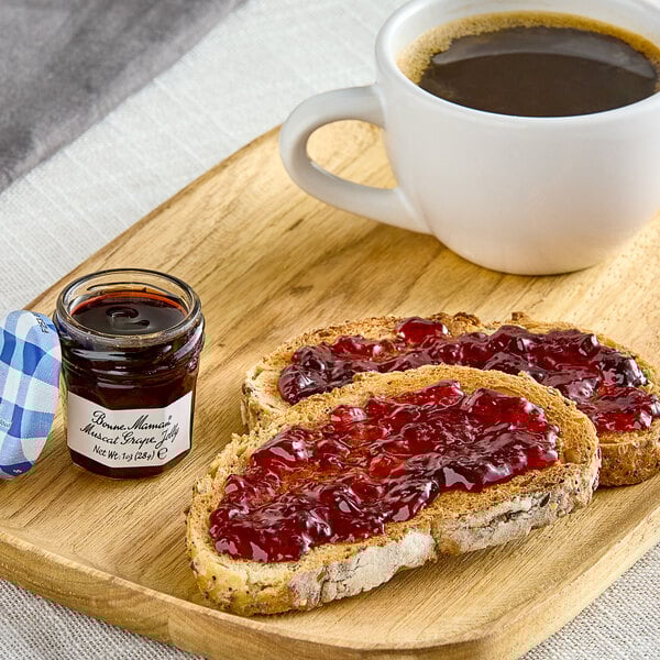 A plate of toast with Bonne Maman Muscat Grape Jelly on it next to a cup of coffee on a table.