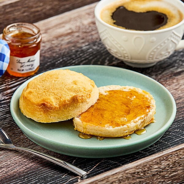 A plate with a biscuit and a mini jar of Bonne Maman honey on a table in a breakfast diner.