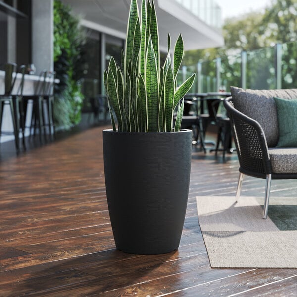 A Lancaster Table & Seating black planter with a potted plant on a wood floor.