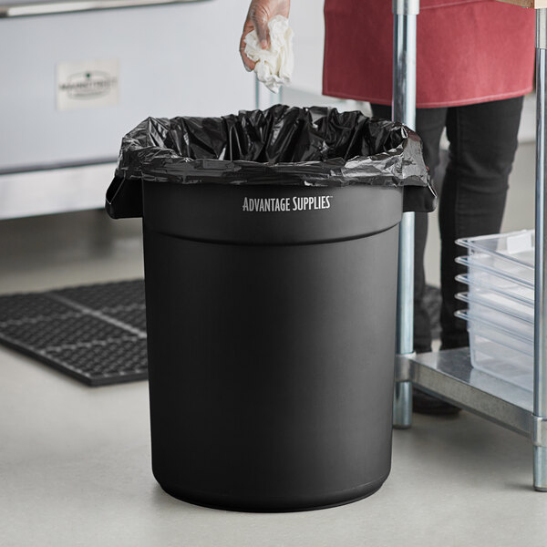 A woman holding a white towel over a black Advantage Supplies trash can.