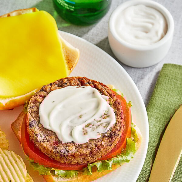 A plate with a burger, chips, and a white container of Sir Kensington's Vegan Mayonnaise.